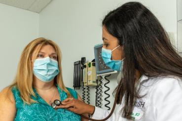 Cardiologist Anupama Rao, MD, uses a stethoscope to check a woman patient's heart beat.